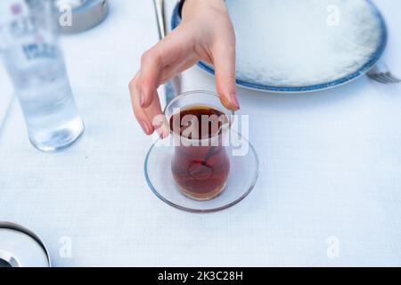 Frau hält türkischen Tee, türkischer Raki im Hintergrund, Putenpub und traditionelles Raki-Drink-Konzept, Sitzansicht, türkische Getränkeidee Stockfoto