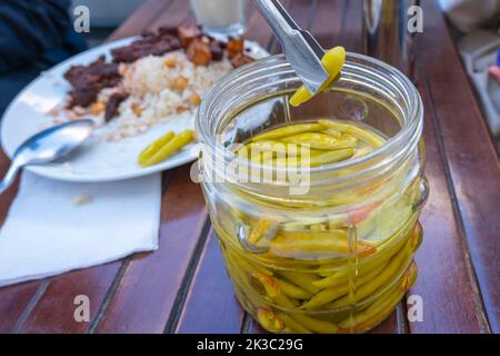 Pflücken eingelegter Paprika aus dem Glas, türkische traditionelle Gurke, türkische Leber und Reis auf dem Hintergrund, selektiver Fokus Stockfoto
