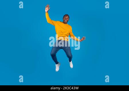 Emotionaler schwarzer Mann im lässigen Springen über blauen Hintergrund Stockfoto