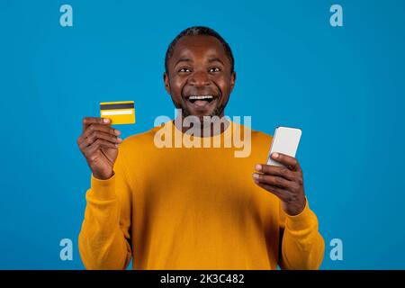 Aufgeregter schwarzer Mann mit Handy und Kreditkarte Stockfoto