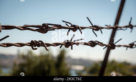Nahaufnahme von Stacheldraht mit blauem Himmel und Landschaft im Hintergrund, Freiheit und Hoffnung Idee, Sicherheit und Schutz, Metalldrähte, Stahl Barbwire Stockfoto