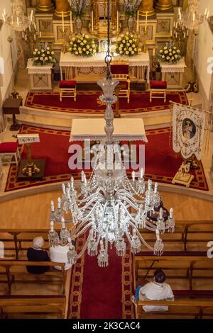 Pilgrim-Glas-Pendelleuchte in der Kirche von Pontevedra mit dem wunderschön beleuchteten Altar im Hintergrund und Kirchenbänken mit Betenden Stockfoto