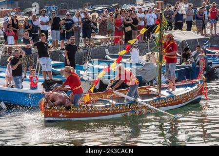 Das jährliche Fest der 'U Pisci a Mari' im sizilianischen Dorf Aci Trezza, in der Nähe von Catania. Dies findet um das Fest der Geburt des hl. Johannes des Täufers Ende Juni statt. Es handelt sich um eine traditionelle Fischereiexpedition für Schwertfisch, die früher in der Straße von Messina stattgefunden hat. Die Rolle des Schwertfisches wird von einem Schwimmer gespielt, der wiederholt von den Fischern gefangen wird, blutig aufgeschnitten wird, dann aber irgendwie entkommen kann. Schließlich schafft es der „Schwertfisch“, das Boot umzustürzen. Stockfoto