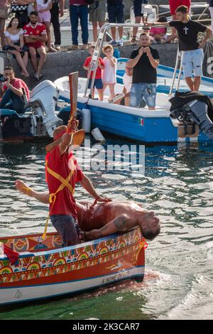 Das jährliche Fest der 'U Pisci a Mari' im sizilianischen Dorf Aci Trezza, in der Nähe von Catania. Dies findet um das Fest der Geburt des hl. Johannes des Täufers Ende Juni statt. Es handelt sich um eine traditionelle Fischereiexpedition für Schwertfisch, die früher in der Straße von Messina stattgefunden hat. Die Rolle des Schwertfisches wird von einem Schwimmer gespielt, der wiederholt von den Fischern gefangen wird, blutig aufgeschnitten wird, dann aber irgendwie entkommen kann. Schließlich schafft es der „Schwertfisch“, das Boot umzustürzen. Stockfoto