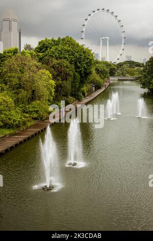 Singapur, 24. Juli 2022 - Wasserfontänen am Kanal mit Riesenrad im Hintergrund. Stockfoto