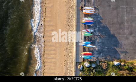 Ein Blick auf den Sonnenaufgang an der Goldküste von Long Island, New York, über den leeren Strand mit farbenfrohen Kajaks Stockfoto