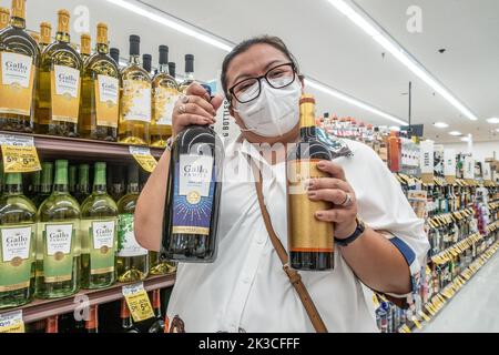 Eine Dame, die in einem Supermarkt in Kalifornien Wein kauft, posiert mit großen Flaschen Wein vor dem Regal. Stockfoto