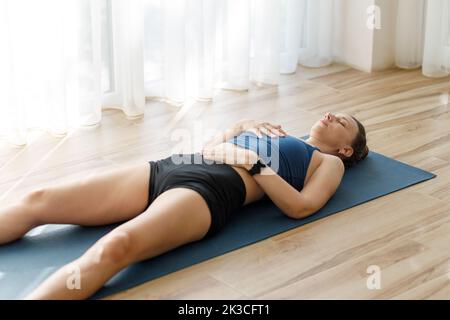 Junge Frau, die sich nach ihrem morgendlichen Fitnessprogramm in Shavasana- oder Leiche-Yoga-Pose entspannt Stockfoto