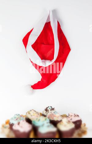 santa Hut hängt auf weißem Hintergrund auf etwas Cupcake Stockfoto