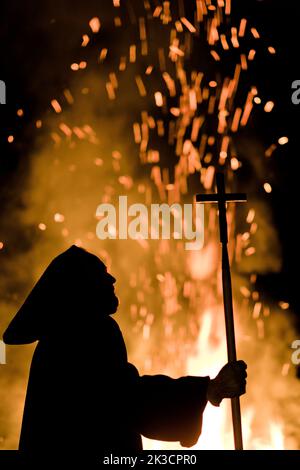 Silhouette eines mittelalterlichen Mönchs, der das Kreuz durch ein wütende Feuer hält Stockfoto