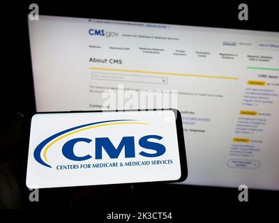 Person, die das Smartphone mit dem Logo der Center for Medicare and Medicaid Services (CMS) auf dem Bildschirm vor der Website hält. Konzentrieren Sie sich auf die Telefonanzeige. Stockfoto