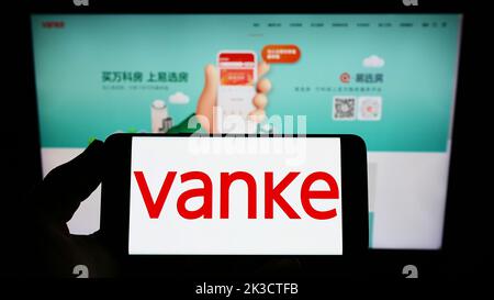 Person, die Smartphone mit dem Logo der chinesischen Immobilienfirma Vanke Co. Ltd. Auf dem Bildschirm vor der Website hält. Konzentrieren Sie sich auf die Telefonanzeige. Stockfoto