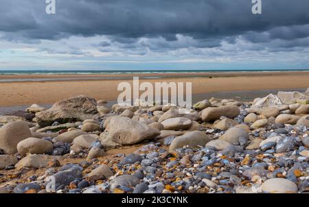 Ebbe am französischen Strand mit vielen Steinen Stockfoto