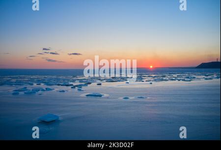 Luftaufnahme des Sonnenuntergangs über dem gefrorenen Meer. Winterlandschaft an der Küste während der Dämmerung. Blick von oben auf das schmelzende Eis im Ozean bei Sonnenaufgang mit Horizont Stockfoto