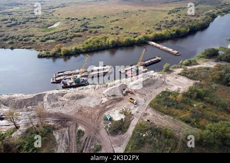 Flussbagger arbeiten am Fluss und entladen Sand von Lastkähnen. Stockfoto
