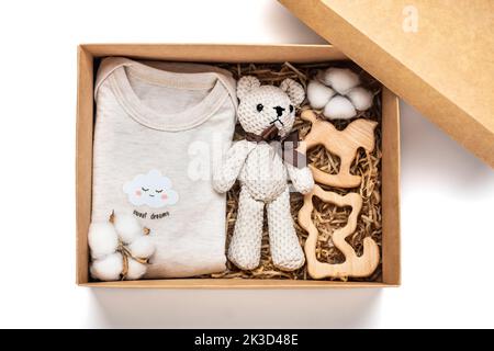 Geschenkkorb mit geschlechtsneutralem Babykleid und Accessoires. Pflegebox aus Bio-neugeborener Baumwolle Kleidung, Teddy, Baumwolle in Box auf weißem Hintergrund Flat Lay Draufsicht. Stockfoto