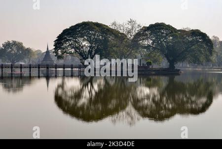 Wunderschöne Morgenansicht des Wat Traphang Ngoen Tempels bei Sonnenaufgang im Sukhothai Historical Park, Thailand. Alte Bäume spiegeln sich wie ein Spiegel auf dem Wasser. Stockfoto