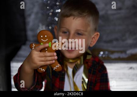 Liebenswert glücklich kaukasischen Kind mit Lebkuchen und macht einen lustigen Gesichtsausdruck. Stimmungsvolles, ästhetisches Weihnachtshaus für Silvester. Fröhlich Stockfoto