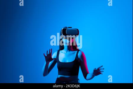 Metaverse Technologiekonzept. Selbstbewusste Brünette junge Frau in Virtual-Reality-Headset in der Luft zeigen, während in einem Studio Raum stehen. Mit VR Stockfoto