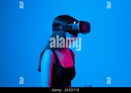 Selbstbewusste Brünette junge Frau in Virtual-Reality-Headset in der Luft zeigen, während in einem Studio Raum stehen. Verwendung von VR-Technologien. Stockfoto
