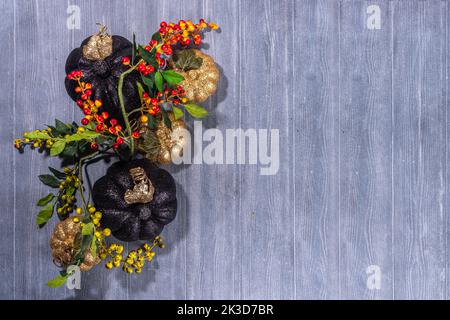 Schwarze und kaltfarbene Kürbisse auf grauem Holzhintergrund. Minimalistischer Stil Halloween Thanksgiving Hintergrund Kopie Raum Stockfoto