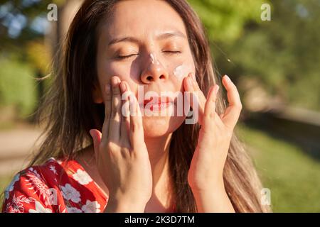 Frau mit Sonnencreme. Junge Latina Putting Hautpflegecreme auf ihr Gesicht. Stockfoto