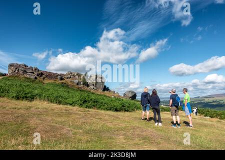 Eine Gruppe von Menschen, die die Cow und Calf Rocks auf Ilkley Moor an einem Sommertag in West Yorkshire, England, bewundern Stockfoto