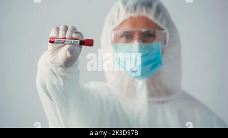 Verschwommener Arzt im Hazmat-Anzug mit negativem Coronavirus-Test isoliert auf grauem Stockbild Stockfoto