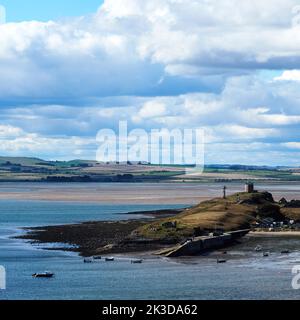 Ein weitläufiger Blick auf den Hafen von Lindisfarne und die Boote, die er schützt, unter einem riesigen Himmel und mit den Hügeln des Festlandes am Horizont. Stockfoto