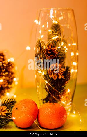 Mandarinen, Zapfen in einer Glasvase und Girlanden auf dem Tisch Stockfoto