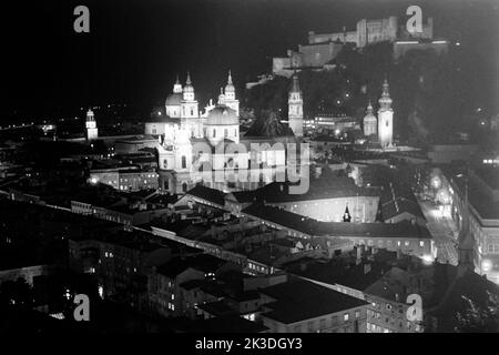 Blick auf das nächtliche Salzburg vom Mönchsberg aus mit Universität und Sacellum, der Kollegienkirche, hinten links dem Salzburger Glockenspiel, daneben der Dom, die Franziskanerkirche, die Türme der Erzabtei Sankt Peter und im Hintergrund die Festung Hohensalzburg, um 1960. Blick auf Salzburg bei Nacht vom Mönchsberg mit der Universität und dem Sacellum, der Kollegienkirche, hinten links das Salzburger Glockenspiel, daneben der Dom, die Franziskanerkirche, die Türme der Erzabtei St. Peter und im Hintergrund die Festung Hohensalzburg, um 1960. Stockfoto