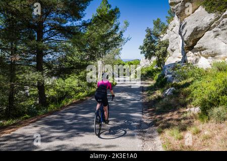 Radfahrerin auf einer ruhigen Landstraße in den Alpilles in der Nähe von Saint-Rémy-de-Provence, Frankreich. Stockfoto