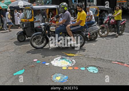 Mumbai, Indien. 26. September 2022. Motorradfahrer fahren in Mumbai an einem in verschiedenen Farben lackierten Schlagloch vorbei. Demonstranten malten Schlaglöcher auf der Straße in verschiedenen Farben als Zeichen des Protests gegen die Brihanmumbai Municipal Corporation (BMC), um ihnen die Verschwendung von Kraftstoff, Staus und den Verlust von Menschenleben durch Schlaglöcher auf den Straßen der Stadt zu merken. (Foto von Ashish Vaishnav/SOPA Images/Sipa USA) Quelle: SIPA USA/Alamy Live News Stockfoto