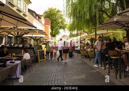 Ljubljana, Slowenien - September 3. 2022. Eine verkehrsreiche Fußgängerzone mit Bars und Restaurants an der Uferpromenade des Flusses Ljubljanici Stockfoto