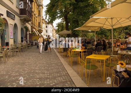 Ljubljana, Slowenien - September 3. 2022. Eine verkehrsreiche Fußgängerzone mit Bars und Restaurants an der Uferpromenade des Flusses Ljubljanici Stockfoto