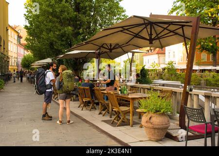 Ljubljana, Slowenien - September 3. 2022. Eine verkehrsreiche Fußgängerzone mit Bars und Restaurants an der Uferpromenade des Flusses Ljubljanici Stockfoto