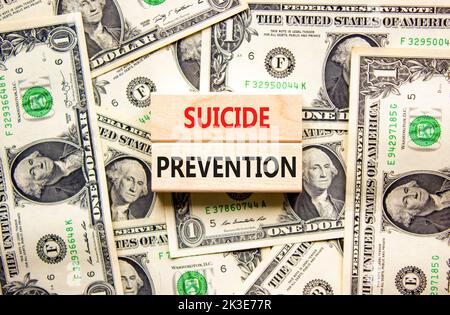 Symbol für die Suizidprävention. Konzept Wörter Selbstmordprävention auf Holzblöcken. Schöner Hintergrund von Dollarscheinen. Dollarscheine. Psychologische und Stockfoto
