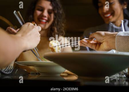 Eine multiethnische Gruppe lächelnder junger Freunde, die im Fusion Bar Restaurant Dim Sum Knödel essen - Nahaufnahme der Essstäbchen, die das Essen pflücken - Essen und Stockfoto