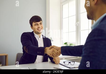 Zwei lächelnde Geschäftsleute, die sich nach der Vertragsunterzeichnung im Büro die Hände schüttelten. Stockfoto