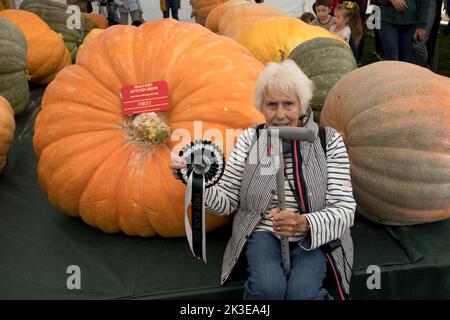 Frau, die an riesigen Kürbissen sitzt, ist ein Teil des riesigen Gemüses auf der Three Counties Autumn Show Great Malvern, Großbritannien Stockfoto