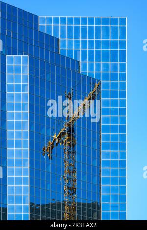 Hoher gelber Kran, der auf einem Wolkenkratzer mit Glasfenstern reflektiert, die durch den klaren Sommerhimmel blau gemacht wurden Stockfoto