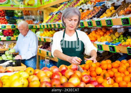 Weibliche Supermarktarbeiterin stapelt Früchte im Verkaufsraum auf dem Regal Stockfoto