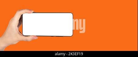 Handy-Mockup mit horizontaler Ausrichtung in der Hand zeigt Werbung mobile Smartphone-App auf orangefarbenem Banner Hintergrund. Hochwertige Fotos Stockfoto