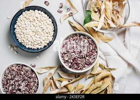 Frisch geerntete weiße und rote Bohnen in Schüsseln, Draufsicht. Stockfoto