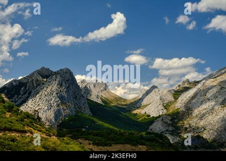 alpine Landschaft, felsige Gipfel unter blauem Himmel, Mittagslichter mit Schatten, die durch die Täler und ihre Wälder ziehen Stockfoto