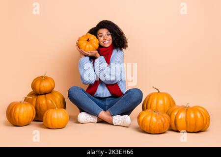 Portrait von attraktiven fröhlich lustig niedlich trendy Mädchen hält umarmenden Kürbis isoliert über beige Pastellfarbe Hintergrund Stockfoto