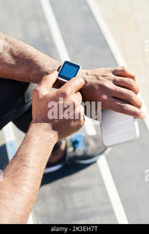 Nahaufnahme der Hände eines jungen afroamerikanischen Sportlers, der auf der Armbanduhr Zeit notiert, während er auf der Treppe sitzt und sich nach dem Training ausruhen kann Stockfoto