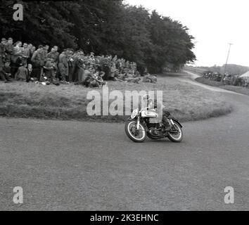 1954, historisch, in einem bewaldeten Teil eines Waldes, beobachten Zuschauer auf einem grasbewachsenen Hügel, wie ein Rennfahrer auf einem Norton-Motorrad eine Kurve auf dem Kurs bei den Scarborough-Rennen, England, macht. Die berühmte Oliver’s Mount Road Rennstrecke ist Englands einzige natürliche „Road“ Rennstrecke, bekannt als „Mini TT“. Die anspruchsvolle, hügelige Strecke liegt in der Nähe von Scarboroughs Strandpromenade, weshalb die Veranstaltung traditionell als Scarborough Races bekannt war. Stockfoto