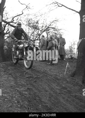 1954, historisch, draußen auf unwegsamem Gelände in einem Wald, Zuschauer beobachten einen Konkurrenten (Nr. 54), der ein Motorrad der Ära, eventuell ein Ariel, bei einem Gerangel- oder Testrennen in Seacroft, Leeds, England, Großbritannien, organisiert vom West Leeds Motor Club, fährt. Stockfoto