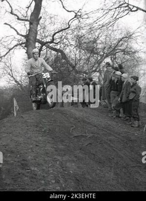 1954, historisch, draußen auf unwegsamem Gelände in einem Wald, Zuschauer beobachten einen Konkurrenten, der ein Motorrad der Ära, ein Ariel, in einem Gerangel oder Proberennen in Seacroft, Leeds, England, Großbritannien, organisiert vom West Leeds Motor Club, fährt. Stockfoto